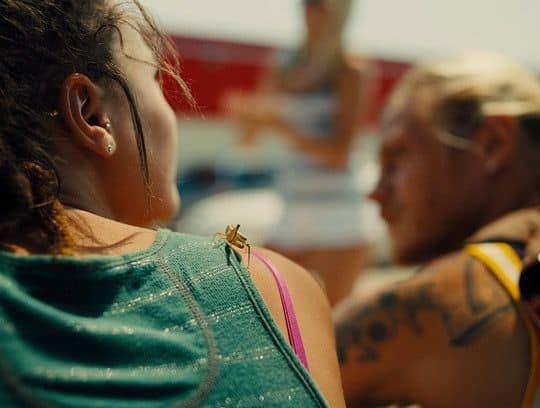 Star and Corey, sunlit moment – Star leans toward Corey outside in the golden light, their heads close in quiet conversation, the summer heat visible on their skin.