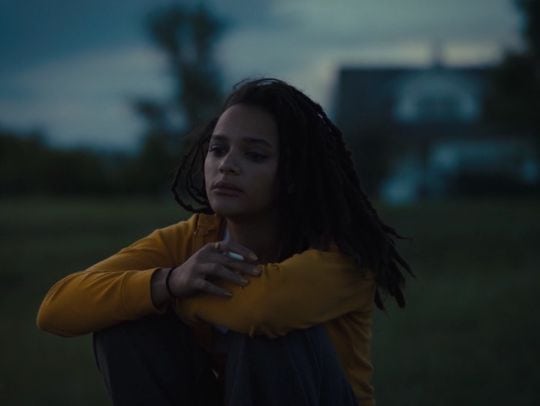 Arms crossed in field – Star sits alone in an open field, arms wrapped around herself in a yellow sweatshirt, framed by dusk tones.