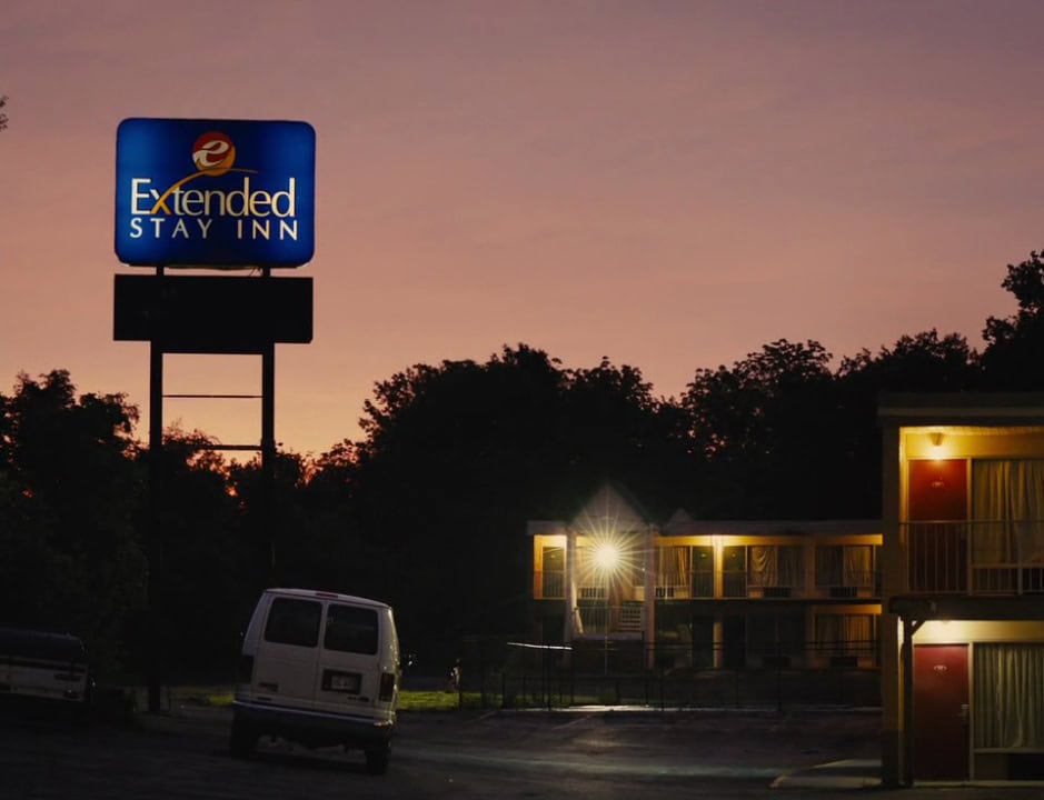 Motel sign – A blue Baymont Inn motel sign glows against a fading pink sunset sky, with the motel and van below bathed in shadow.